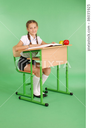 Girl in a school uniform sitting at a desk and reading a book 86035925