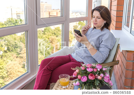 Young woman on a balcony listening music or talking by phone Young woman on a balcony listening music or talking by phone 86036588