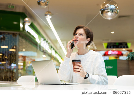 Young attractive woman sitting at a shopping center at a table and working at a computer laptop 86037555