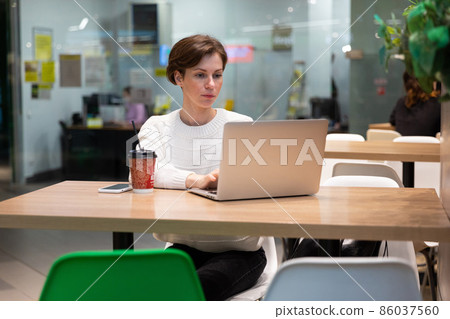 A photo of a young woman who sits at the food court of a shopping center at a table and works at a 86037560