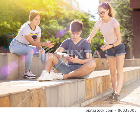 Company of teenagers with smartphones are communicating on walk 86038305