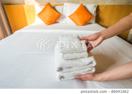 Close-up of hotel maid arranging the stack of towels on bed. Conceptual of female chambermaid making bed in hotel room. Close-up of hotel maid arranging the stack of towels on bed. Conceptual of female chambermaid making bed in hotel room. 86041862