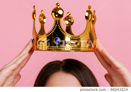 Unknown woman putting on golden crown, arrogance and privileged status, concept of self confidence in success, self-motivation and dreams to be best. Indoor studio shot isolated on pink background. Unknown woman putting on golden crown, arrogance and privileged status, concept of self confidence in success, self-motivation and dreams to be best. Indoor studio shot isolated on pink background. 86043824