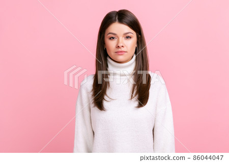 Serious bossy dark haired female looking at camera with strict facial expression, being unhappy, wearing white casual style sweater. Indoor studio shot isolated on pink background. Serious bossy dark haired female looking at camera with strict facial expression, being unhappy, wearing white casual style sweater. Indoor studio shot isolated on pink background. 86044047