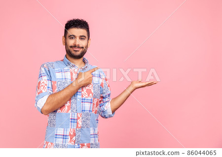 Good looking joyful man with beard in blue shirt presenting advertising area on her palm and pointing to copy space, holding empty place for commercial. Indoor studio shot isolated on pink background. Good looking joyful man with beard in blue shirt presenting advertising area on her palm and pointing to copy space, holding empty place for commercial. Indoor studio shot isolated on pink background. 86044065