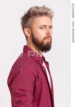 Side view portrait of handsome concentrated bearded young adult man in plaid t-shirt thoughtfully looking to side. Indoor studio shot isolated on gray background Side view portrait of handsome concentrated bearded young adult man in plaid t-shirt thoughtfully looking to side. Indoor studio shot isolated on gray background 86044228