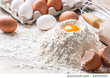 Detail of dough preparation with egg yolk, flour, eggs, rolle and a whisk on a table Detail of dough preparation with egg yolk, flour, eggs, rolle and a whisk on a table 86045900