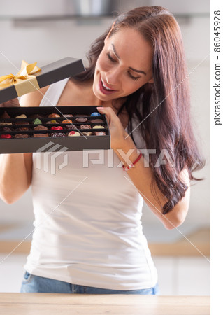 Curious woman peeks inside a chocolate box with selection of various chocolate candies 86045928