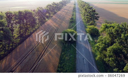 Aerial drone view flight over highway wheat field and green trees at sunset dawn 86047269