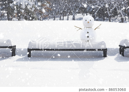 Cute snowman on a snowy park bench 86053068