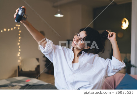 Delighted woman taking selfie on vintage camera in blurred room Delighted woman taking selfie on vintage camera in blurred room 86053525