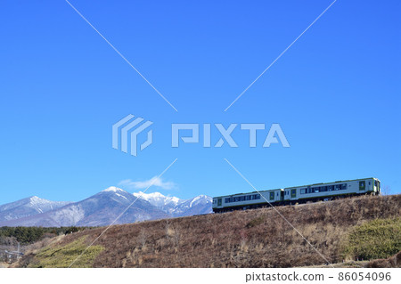 Koumi Line Kiha 110 series railcar running on the embankment with Yatsugatake in the background 86054096