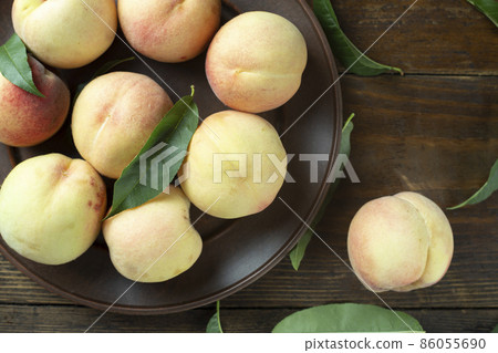 Ripe peaches with leaves in a clay plate on a wooden table. Ripe peaches with leaves in a clay plate on a wooden table. 86055690