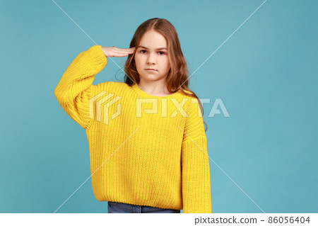 Yes, sir. Portrait of little girl saluting and looking at camera with respect, patriotic child, wearing yellow casual style sweater. Indoor studio shot isolated on blue background. Yes, sir. Portrait of little girl saluting and looking at camera with respect, patriotic child, wearing yellow casual style sweater. Indoor studio shot isolated on blue background. 86056404