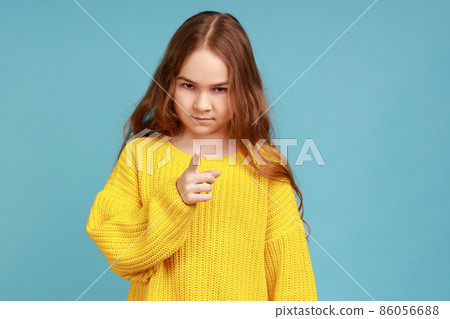 Portrait of little girl standing with admonishing gesture, warning, looking with strict expression, wearing yellow casual style sweater. Indoor studio shot isolated on blue background. Portrait of little girl standing with admonishing gesture, warning, looking with strict expression, wearing yellow casual style sweater. Indoor studio shot isolated on blue background. 86056688