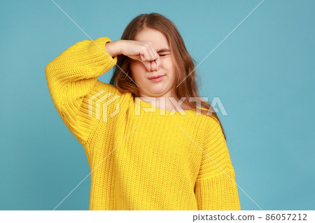 Little girl holding breath, pinching her nose and expressing disgust to stink, intolerable odor, wearing yellow casual style sweater. Indoor studio shot isolated on blue background. Little girl holding breath, pinching her nose and expressing disgust to stink, intolerable odor, wearing yellow casual style sweater. Indoor studio shot isolated on blue background. 86057212