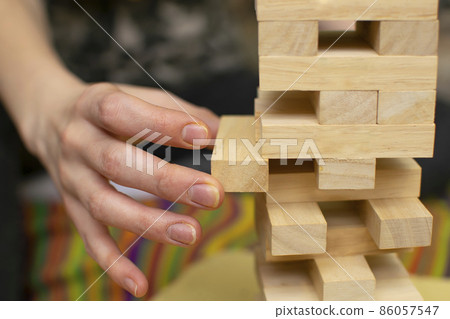 hand of a man, a girl, pulls a piece of wooden bar from the tower structure of a toy house hand of a man, a girl, pulls a piece of wooden bar from the tower structure of a toy house 86057547