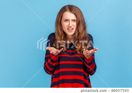 What's the problem. Portrait of irritated indignant woman, raising hands in anger and shouting why how, what do you want, quarreling, wearing sweater. Indoor studio shot isolated on blue background. 86057593