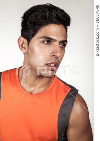 Portrait of tired handsome brunette sporty man wearing orange sports clothing looking away with exhausted facial expression, posing after training. Indoor studio shot isolated on gray background. Portrait of tired handsome brunette sporty man wearing orange sports clothing looking away with exhausted facial expression, posing after training. Indoor studio shot isolated on gray background. 86057649