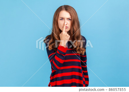 You are liar. Portrait of angry woman wearing striped casual style sweater standing and looking at camera with lie sign, falsehood in communication. Indoor studio shot isolated on blue background. 86057855