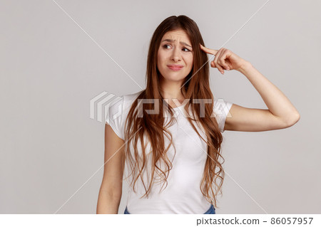 Portrait of displeased woman showing stupid gesture, accusing dumb reckless suggestion, crazy plan for idiots, wearing white T-shirt. Indoor studio shot isolated on gray background. Portrait of displeased woman showing stupid gesture, accusing dumb reckless suggestion, crazy plan for idiots, wearing white T-shirt. Indoor studio shot isolated on gray background. 86057957