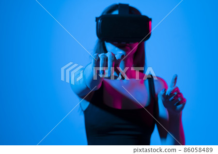 Young woman wearing VR goggles and interacts with cyberspace using swipe and stretching gestures while playing a video game with a friends in metaverse. 86058489