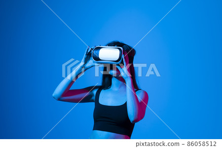 Portrait of woman in vr glasses playing in online video game with her friends in metaverse, in neon light. Virtual reality, technology, entertainment and people. Portrait of woman in vr glasses playing in online video game with her friends in metaverse, in neon light. Virtual reality, technology, entertainment and people. 86058512