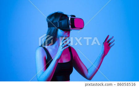 Virtual reality, technology, entertainment and people. Portrait of teen woman in vr glasses playing in online game with 3D simulation, in neon light. 86058516