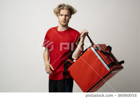Delivery employee man in red t-shirt uniform work as dealer courier and hold red thermal food bag with food isolated on white background studio. Service concept. Delivery employee man in red t-shirt uniform work as dealer courier and hold red thermal food bag with food isolated on white background studio. Service concept. 86060058