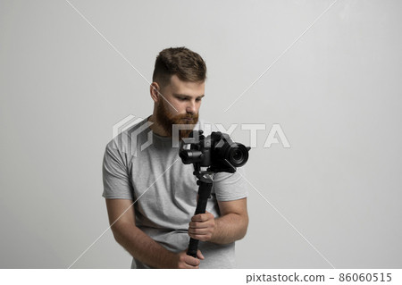 Professional bearded videographer holding camera which set on 3-axis gimbal. Videographer using steadicam. Pro equipment helps to make high quality video without shaking. 86060515