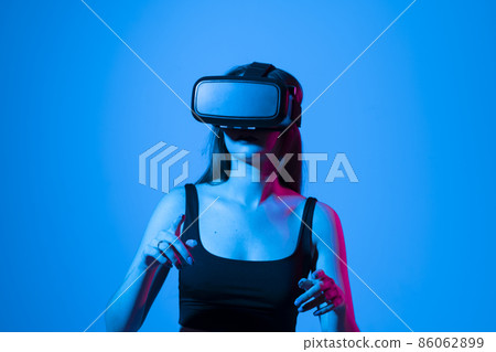Young woman using VR headset helmet to interacts with metaverse using swipe and stretching gestures. Watching virtual reality 3d video. Girl in VR goggles looking around. 86062899