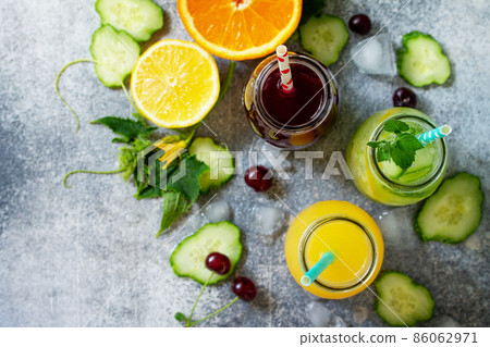 Various refreshments drinks - detox cucumber water, cherry juice and orange juice on stone table. Top view flat lay. 86062971