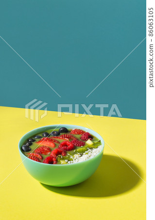 smoothie bowl with fresh berries and fruits in blue plate on yellow dark shadow smoothie bowl with fresh berries and fruits in blue plate on yellow dark shadow 86063105