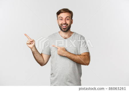 Portrait of excited smiling man with beard, wearing casual gray t-shirt, pointing fingers at upper left corner, showing logo, standing over white background Portrait of excited smiling man with beard, wearing casual gray t-shirt, pointing fingers at upper left corner, showing logo, standing over white background 86063261