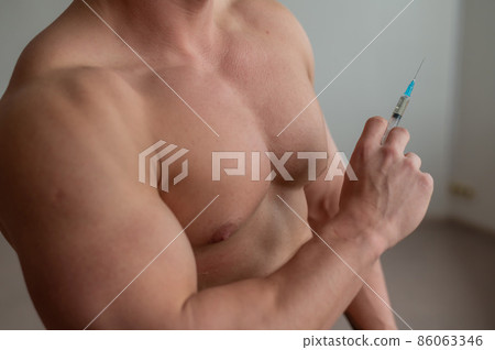 Close-up of a naked male torso. Unrecognizable shirtless bodybuilder man puts himself an injection of testosterone. Faceless athlete takes dope. 86063346