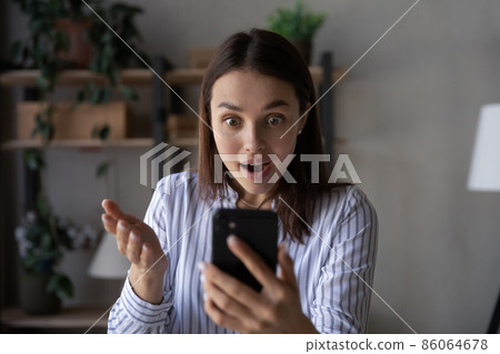 Shocked excited smartphone user staring at mobile phone screen Shocked excited smartphone user staring at mobile phone screen 86064678