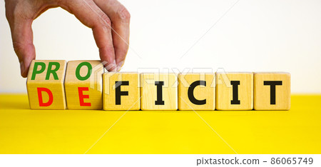 Proficit or deficit symbol. Businessman turns cubes, changes the word deficit to proficit. Beautiful yellow table, white background, copy space. Business, proficit or deficit concept. Proficit or deficit symbol. Businessman turns cubes, changes the word deficit to proficit. Beautiful yellow table, white background, copy space. Business, proficit or deficit concept. 86065749