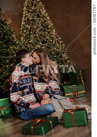 A guy and a girl hug and kiss against the background of a Christmas tree and a red sofa A guy and a girl hug and kiss against the background of a Christmas tree and a red sofa 86065767