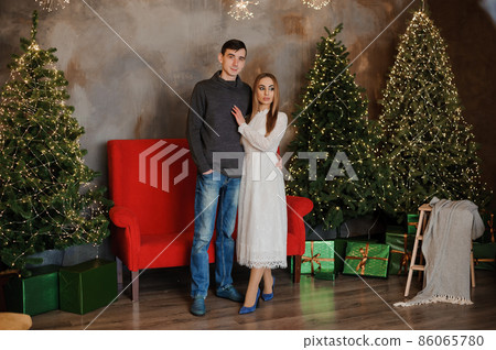 A guy and a girl hug and kiss against the background of a Christmas tree and a red sofa A guy and a girl hug and kiss against the background of a Christmas tree and a red sofa 86065780