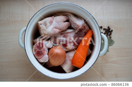 In an old enameled saucepan, raw pork meat and a leg, carrots and onions for making jelly In an old enameled saucepan, raw pork meat and a leg, carrots and onions for making jelly 86066136