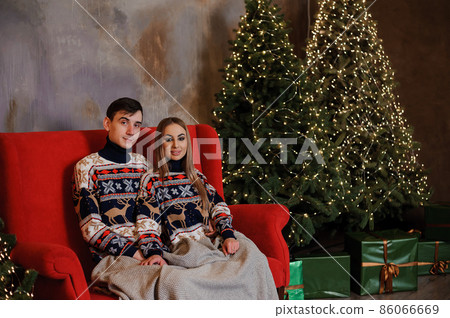 Man and woman sitting on a red sofa and holding a gift Man and woman sitting on a red sofa and holding a gift 86066669