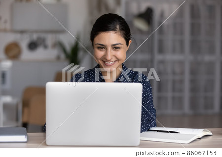 Happy millennial Indian girl working at laptop computer Happy millennial Indian girl working at laptop computer 86067153
