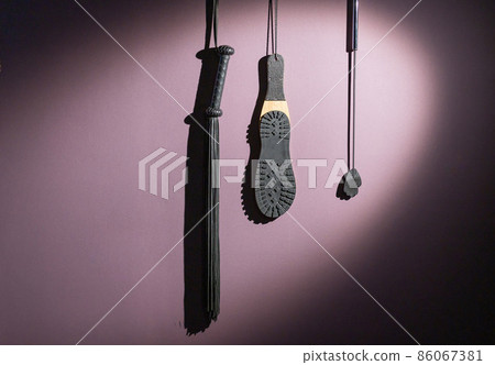 A diverse collection of leather lashes with fringe and a sole for sexual pleasures are hanging on the wall. Sex equipment for punishment and spanking for role-playing games. BDSM room. A diverse collection of leather lashes with fringe and a sole for sexual pleasures are hanging on the wall. Sex equipment for punishment and spanking for role-playing games. BDSM room. 86067381