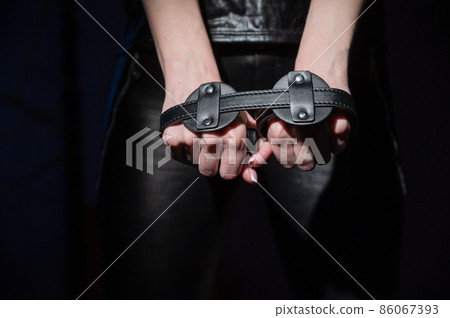 Close-up leather blindfolds in female hands. Unrecognizable woman holds bdsm equipment in the dark. Sexual role-playing games for adults. Humility and dominance. 86067393