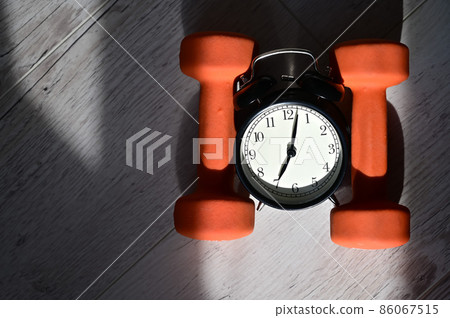 It's time to do sports early in the morning. Top view on alarm clock and orange dumbbells on a wooden floor. It's time to do sports early in the morning. Top view on alarm clock and orange dumbbells on a wooden floor. 86067515