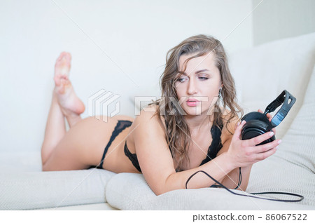 Beautiful woman in black lace underwear lies on her stomach and listens to music. The girl in the bedroom relaxes the bed holds headphones in her hands. Beautiful woman in black lace underwear lies on her stomach and listens to music. The girl in the bedroom relaxes the bed holds headphones in her hands. 86067522