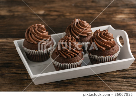 Chocolate cupcakes with chocolate swirl icing on tray on wooden table. Homemade muffins. 86067855