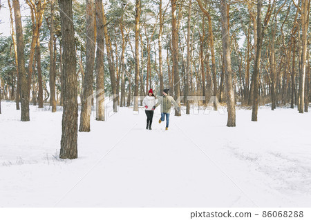 Young boy and girl running in winter park. Young couple are running on sunny day in snowy forest. 86068288