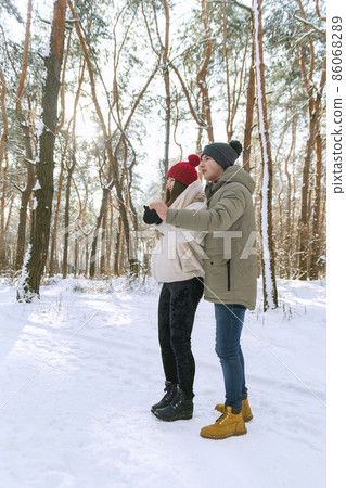 Loving couple walks through winter park. Guy and her girlfriend are enjoying sunny winter day. Side view Loving couple walks through winter park. Guy and her girlfriend are enjoying sunny winter day. Side view 86068289