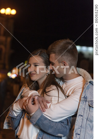 Young couple guy and girl hugging on the background of the night city. Outdoors relationship. Vertical frame Young couple guy and girl hugging on the background of the night city. Outdoors relationship. Vertical frame 86068290